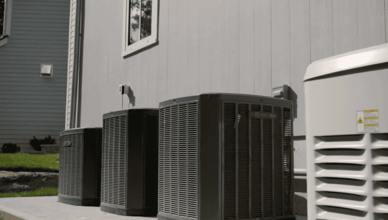 Outdoor AC units lined up beside a residential home, part of a central air conditioning system.
